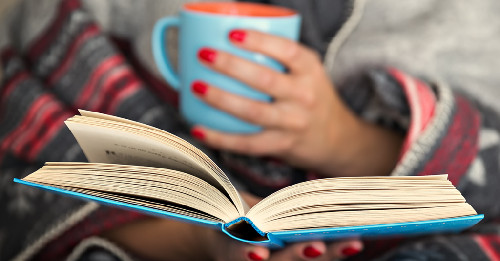 An open book held by a woman holding a mug.