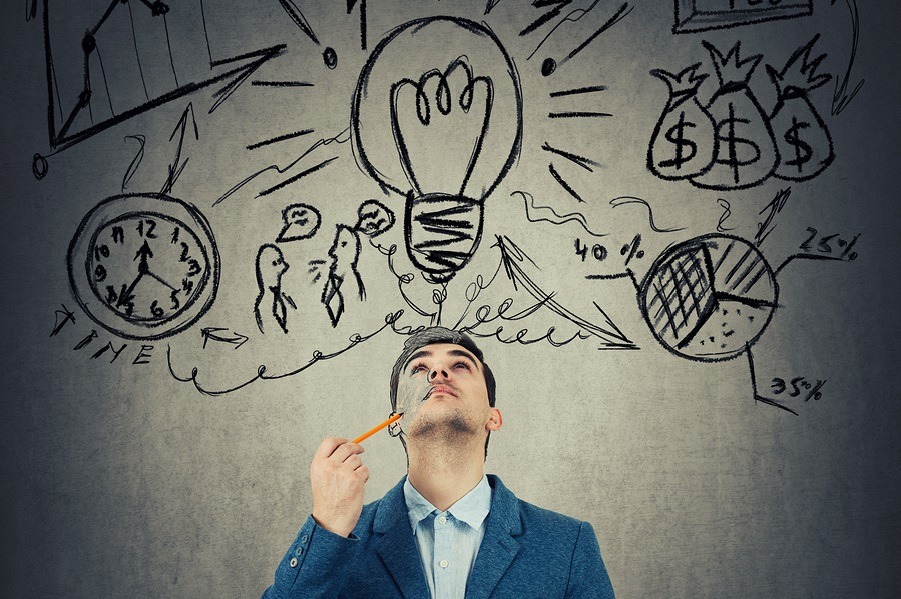 A business professional looking up at sketched ideas and thoughts. He holds a pencil to his cheek.